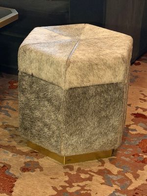 a small stool with a cow hide on it in a living room