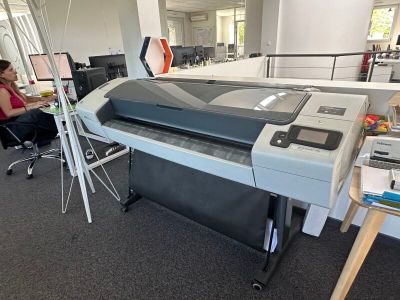 une femme assise à un bureau, à côté d'une grande imprimante
