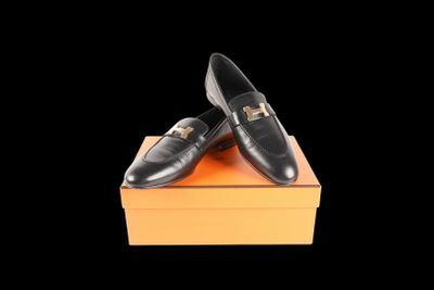 black leather loafers with gold buckles on top of an orange box