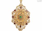 a close up of a gold pendant with a green and red stone