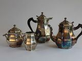 three silver teapots and two silver cups on a table
