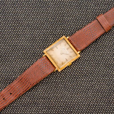 un gros plan d'une montre posée sur une surface noire, avec un bracelet marron