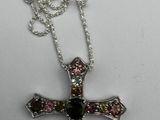 silver cross with multi colored stones on a chain on a white surface