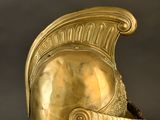 an antique gold helmet on a clear stand against a black background