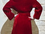 a woman standing in front of a brick wall wearing a red dress