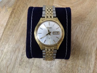 une image représentant une montre-bracelet en or et en argent posée sur une manchette en velours bleu