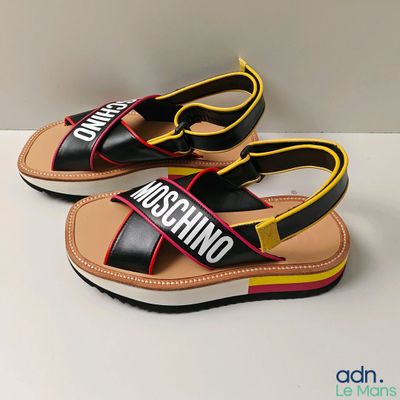 une paire de sandales Moschino noires et jaunes posées sur une surface blanche