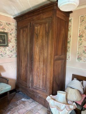 a wooden armoire in the corner of a room with floral wallpaper
