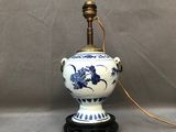 une photo d'une lampe en forme de vase bleu et blanc posée sur un pied noir
