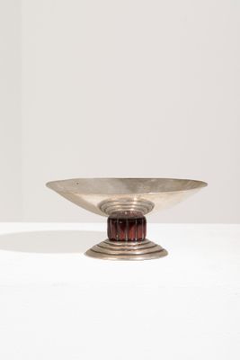 une assiette en argent avec un socle en bois posée sur une surface blanche