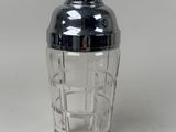 un shaker en verre avec un couvercle noir posé sur une surface blanche