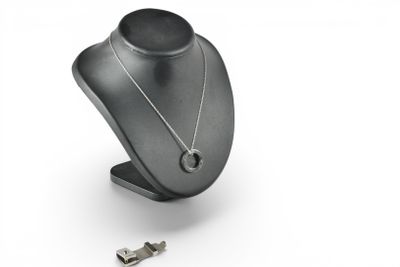 a silver necklace with a key on a stand on a white background