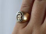 a person ' s hand holding a gold ring with a skull and cross on it