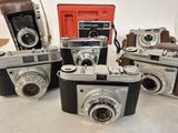 several old cameras are lined up on a table with a red case