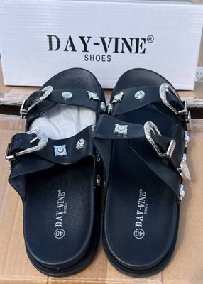 une paire de sandales noires posée sur une boîte en carton, avec une autre boîte en arrière-plan