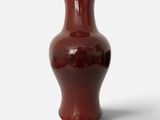 un vase rouge posé sur une surface blanche
