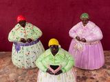 trois figurines représentant des femmes en robes colorées, assises sur une table