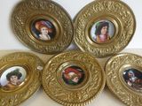 quatre assiettes en or ornées de portraits, posées sur une table