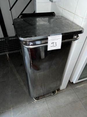 une poubelle sur laquelle est accrochée une pancarte, dans des toilettes