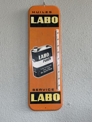 an orange and black sign hanging on a wall with a thermometer on it