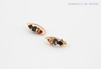 une paire de boucles d'oreilles noires et dorées posées sur une surface blanche