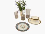 un vase contenant des fleurs, à côté d'une assiette accompagnée d'une tasse et d'une soucoupe