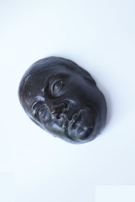 une sculpture noire représentant le visage d'un homme sur une surface blanche
