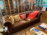un canapé en cuir marron dans un salon où se trouvent de nombreux livres sur la table