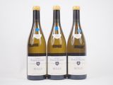 trois bouteilles de vin blanc posées l'une à côté de l'autre sur une surface blanche