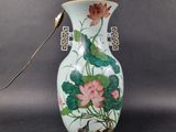 a white vase with a pink flower and green leaves on it
