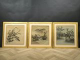 trois peintures chinoises encadrées représentant des montagnes et des arbres, posées sur un parquet