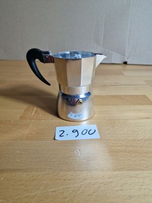 une cafetière en argent posée sur une table en bois, avec une étiquette de prix