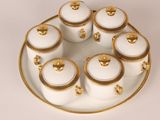 a white and gold plate with six white and gold containers on it