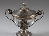 une tasse plaquée argent avec un couvercle en verre, posée sur un socle