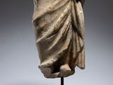 an ancient statue of a woman with a draped dress on a wooden stand