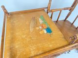 a wooden rocking chair with a painting on the seat