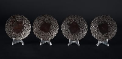 trois plats plaqués argent posés sur des supports, sur fond noir