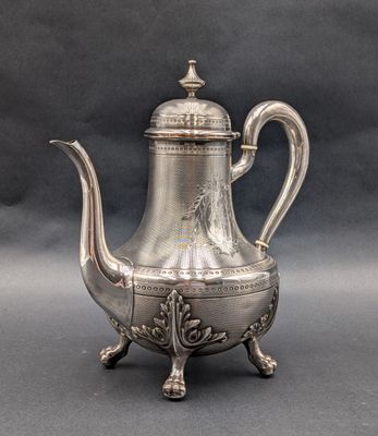 une théière en argent avec une anse, posée sur un socle, sur un fond gris