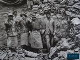 a black and white photo of a group of men standing in front of a pile of clothing