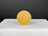 pièce d'or posée sur un socle blanc, sur fond noir