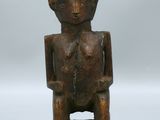 une vieille statue en bois représentant un homme assis sur un socle noir