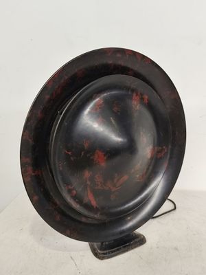 une assiette noire et rouge posée sur un support, sur une surface blanche