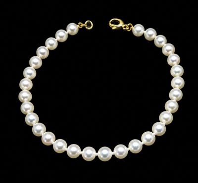 a white pearl necklace with a gold clasp on a black background