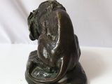 bronze statue of a monkey sitting on a rock with its head on the ground