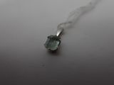 a close up of a necklace with a green stone on a white surface