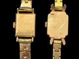 two gold colored watches sitting next to each other on a black surface