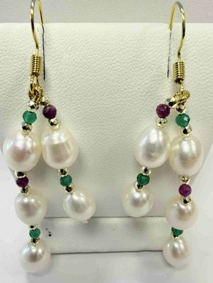 des boucles d'oreilles en perle blanche et émeraude exposées dans une vitrine