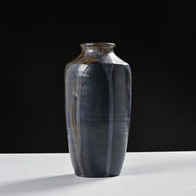 un vase noir posé sur une table blanche, sur fond noir