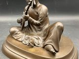 bronze statue of a woman playing a flute on a marble base