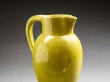 un vase jaune posé sur une surface grise, avec une ombre au sol